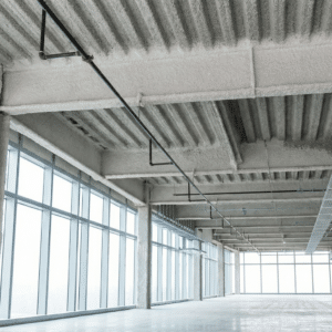 Spray-applied fireproofing (SFRM) coating on structural steel beams, deck, and columns in an empty commercial building interior with floor-to-ceiling windows