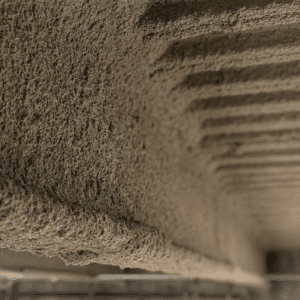 Close-up of spray-applied fire-resistive material SFRM on structural steel beam showing cementitious texture and thickness