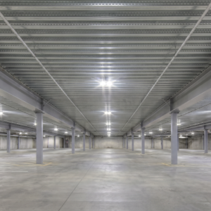 Empty multi-level parking garage interior with exposed corrugated steel deck ceiling, intumescent fireproofing coating steel columns, and bright LED lighting stretching the length of the structure.