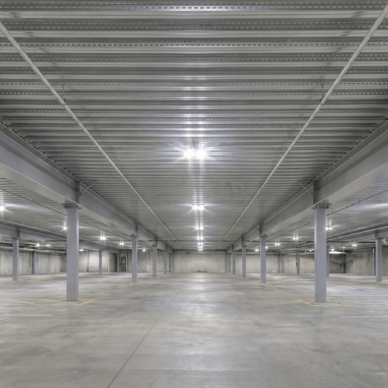 Empty multi-level parking garage interior with exposed corrugated steel deck ceiling, intumescent fireproofing coating steel columns, and bright LED lighting stretching the length of the structure.