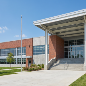 Full descriptive version (recommended for blog): Modern K-12 school building exterior with brick facade, large windows, and steel-framed entry canopy on a clear day, showing institutional construction typical of educational facilities requiring fireproofing and code compliance.