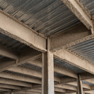 Spray applied fireproofing on a steel structure of a commercial building, brown or beige in color and porous and rough.