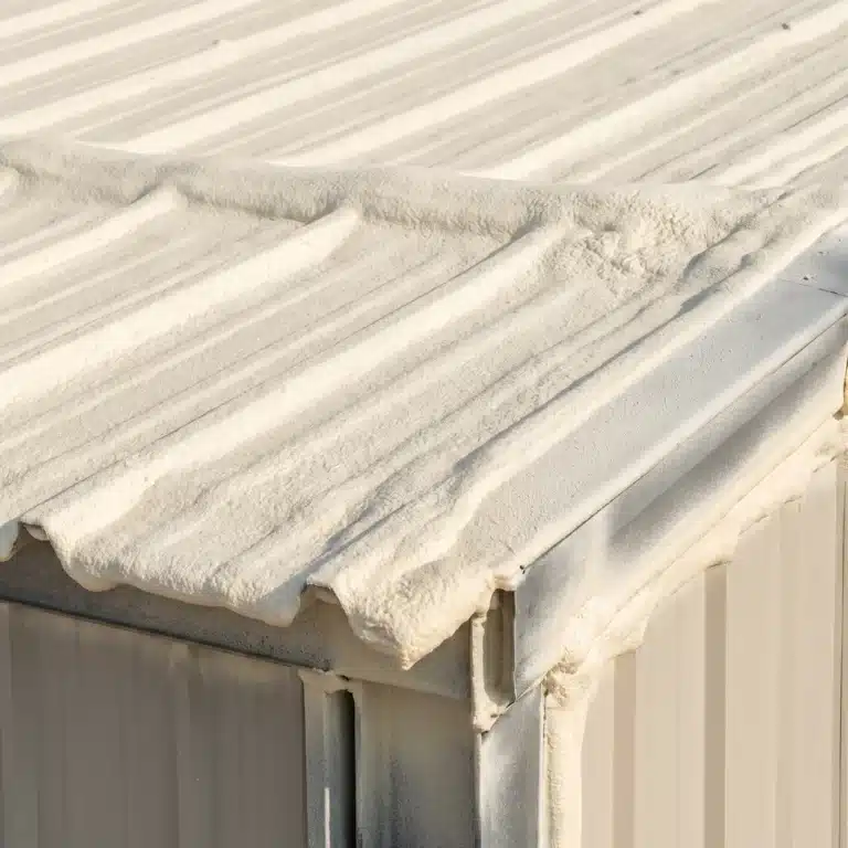 Vapor barrier: closed-cell spray foam carried continuously over a metal roof deck and down the wall at an eave corner
